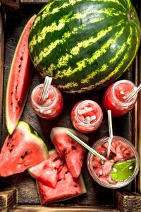 a whole watermelon displayed with sliced melon and glasses of juice